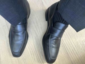Photo of Black Ribbed Southern Scholar socks with grey slacks and black To Boot Loafers